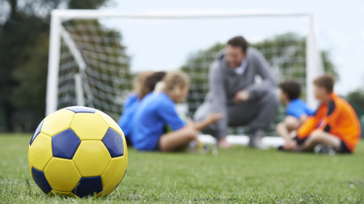 Coach  And Team Discussing Soccer Tactics With Ball In Foreground