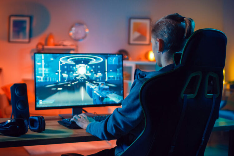Back Shot of a Gamer Playing First-Person Shooter Online Video Game on His Powerful Personal Computer. Room and PC have Colorful Neon Led Lights. Cozy Evening at Home.