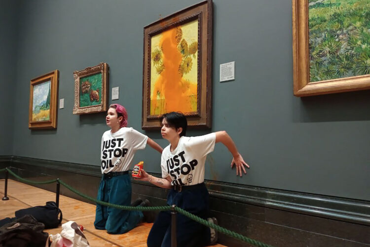 A handout picture from the Just Stop Oil climate campaign group shows activists with their hands glued to the wall under Vincent van Gogh's "Sunflowers" after throwing tomato soup on the painting at the National Gallery in central London on October 14, 2022. - London's Metropolitan Police said its officers arrested two protesters from the Just Stop Oil group for criminal damage and aggravated trespass after they "threw a substance over a painting" at the gallery on Trafalgar Square. (Photo by Handout / Just Stop Oil / AFP) / RESTRICTED TO EDITORIAL USE - MANDATORY CREDIT "AFP PHOTO /  JUST STOP OIL " - NO MARKETING - NO ADVERTISING CAMPAIGNS - DISTRIBUTED AS A SERVICE TO CLIENTS