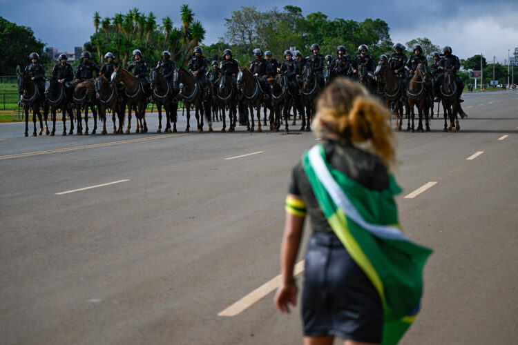 A demonstrator looks at mounted police forces while soldiers dismantle a camp by supporters of Brazil's far-right ex-president Jair Bolsonaro that had been set up in front of the Army headquarters in Brasilia, on January 9, 2023, a day after backers of the ex-president invaded the Congress, presidential palace and Supreme Court. - Brazilian security forces locked down the area around Congress, the presidential palace and the Supreme Court Monday, a day after supporters of ex-president Jair Bolsonaro stormed the seat of power in riots that triggered an international outcry. Hardline Bolsonaro supporters have been protesting outside army bases calling for a military intervention to stop Lula from taking power since his election win. (Photo by Mauro PIMENTEL / AFP)