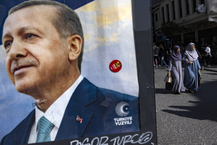 Women walk behind a campaign poster of Turkish President and candidate for his reelection Recep Tayyip Erdogan in Istanbul on May 22, 2023, ahead of on May 28 Turkeyís presidential run-off. The removal of religious restriction in the mostly Muslim but officially secular republic turned the Turkish Islamic-rooted leader into a hero among Turkey's conservatives. His support among housewives, who now have the legal right to stay veiled at school and work, reached 60 percent in the last election in 2018, according to an Ipsos survey, nearly eight points above his national vote. (Photo by Yasin AKGUL / AFP)
