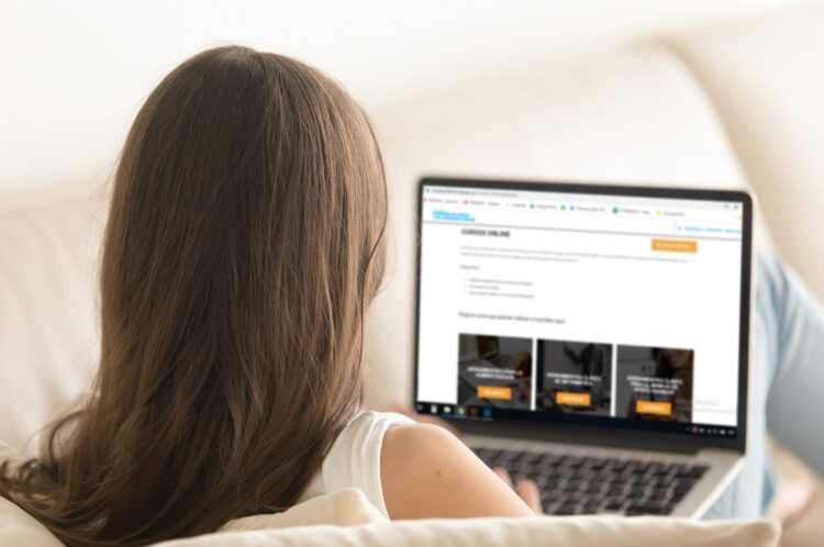 Woman lying on sofa with laptop distantly working from home. Female user browses Internet online, communicates in social network, surfing important information. View over the shoulder close up photo