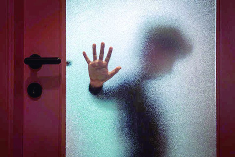 Blurred sad boy leaning open hand against glass door.