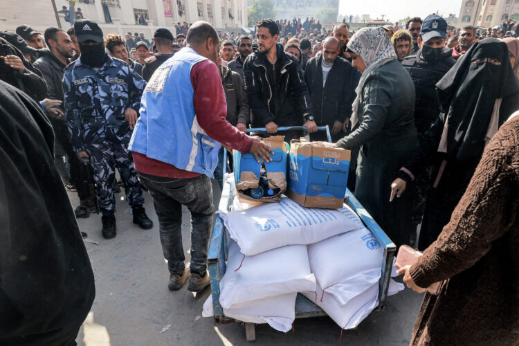 Workers of the United Nations Relief and Works Agency for Palestine Refugees (UNRWA) hand out flour rations and other supplies to people at an UNRWA warehouse in Rafah in the southern Gaza Strip on December 12, 2023, amid continuing battles between Israel and the militant group Hamas. (Photo by MOHAMMED ABED / AFP)