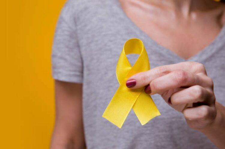 Woman with yellow ribbon on color background. Cancer awareness concep