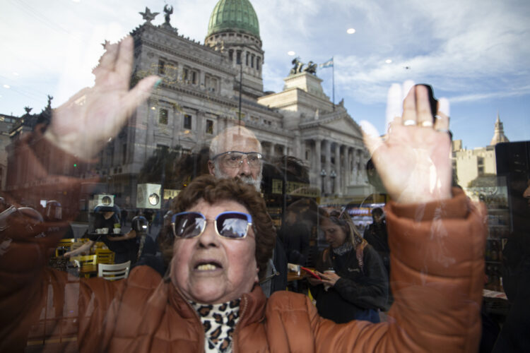 Una jubilada se refugia en un bar de la represión policial, de fondo se refleja el Congreso. Foto: Patry Cugat.