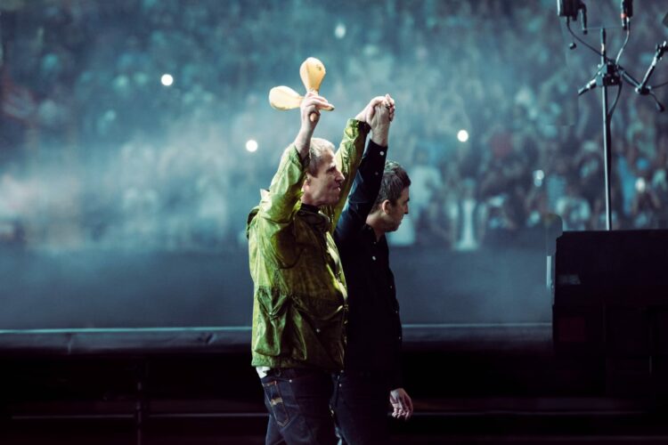 Los hermanos Liam y Noel Gallagher tomados de la mano en su primer show en Cardiff.