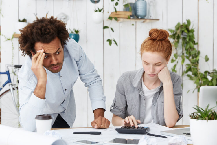 Young mixed race family calculating debts being frustrated. Afro American man being stressed while helping his wife with calculations isolated over home interior. People, finances and paperwork.