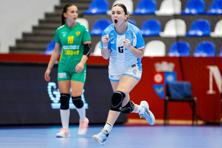 An athlete in a blue and white uniform celebrates with clenched fists while another player in green watches from behind on an indoor sports court.