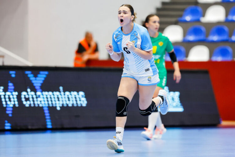 An athlete in a light blue and white uniform celebrates with a raised fist during an indoor handball game.