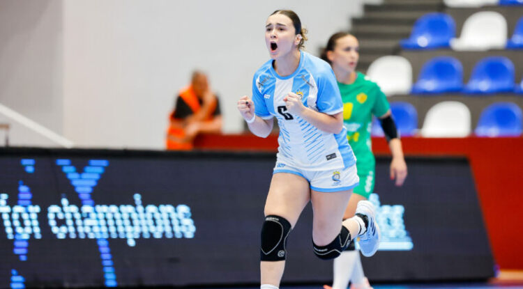 An athlete in a light blue and white uniform celebrates with a raised fist during an indoor handball game.