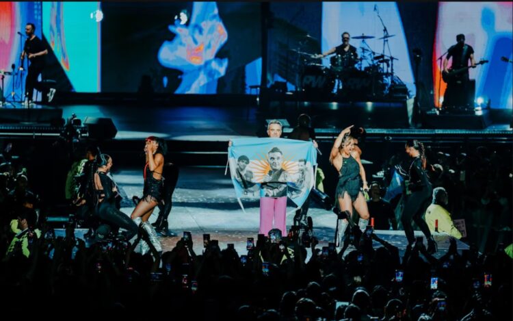 Robbie Williams cerró su regreso al país con “Wonderwall” y presencia cordobesa Robbie Williams mostró una bandera con su rostro, Maradona y Messi. Foto: redes.